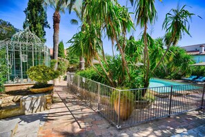 A pool area with a metal fence, palm trees, and a birdcage.