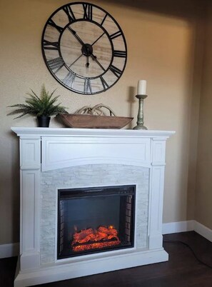 A fireplace with a white mantel, a large wall clock, a potted plant, and a candle holder.