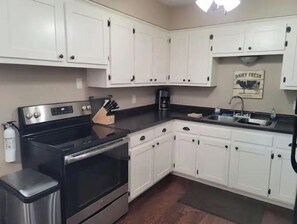Kitchen area with stainless steel stove, oven, coffee maker, and trash bin.