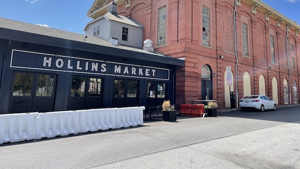 Um edifício de tijolos com uma placa que diz "HOLLINS MARKET" e um carro branco estacionado na frente.