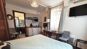 Et kompakt hotelværelse med seng, skrivebord, stol, tekøkken og fjernsyn.