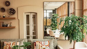 Een zithoek met een bank, fauteuils, een rode stoel, een salontafel en een potplant. Op de vloer ligt een kamerkleed met een patroon en aan de muur hangen decoratieve borden.