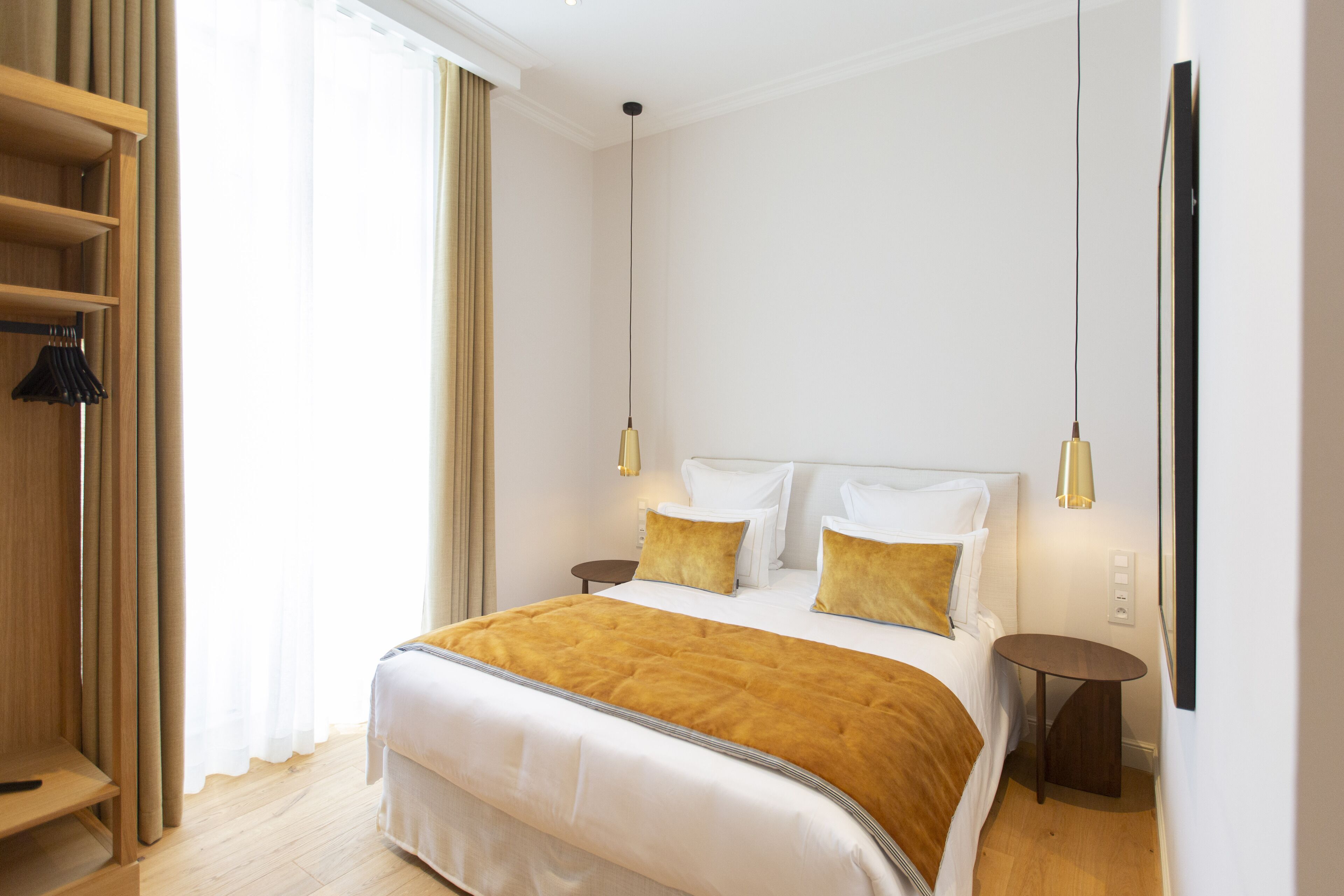 Habitación de hotel con una cama grande, dos mesitas de noche, un armario y una ventana con cortinas.