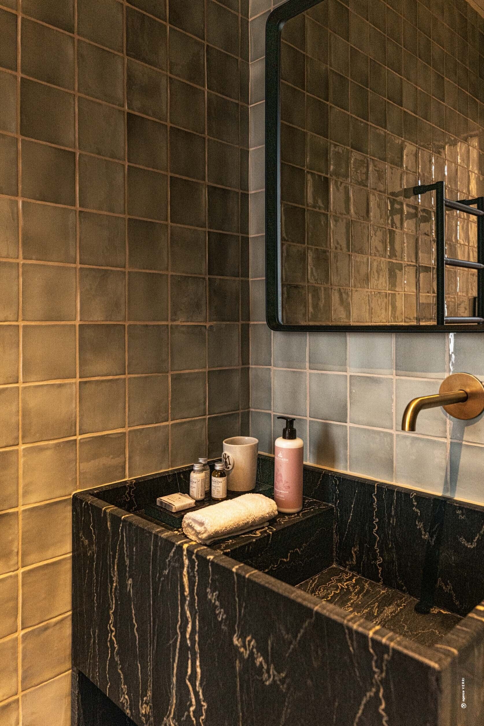 Een badkamer met een zwart marmeren wastafel, een spiegel en toiletartikelen op het aanrecht.