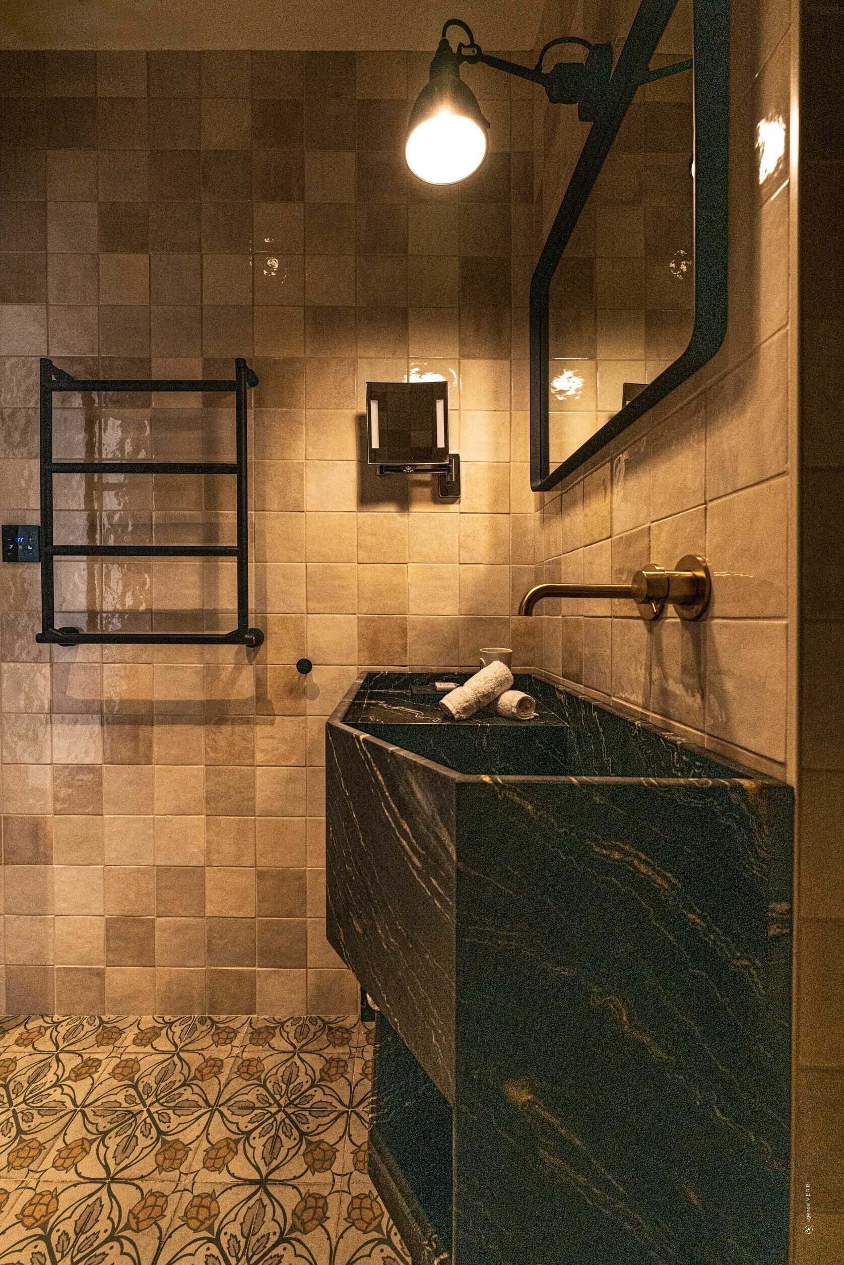 Une salle de bain avec un lavabo en marbre, un porte-serviettes, un miroir et une pomme de douche.