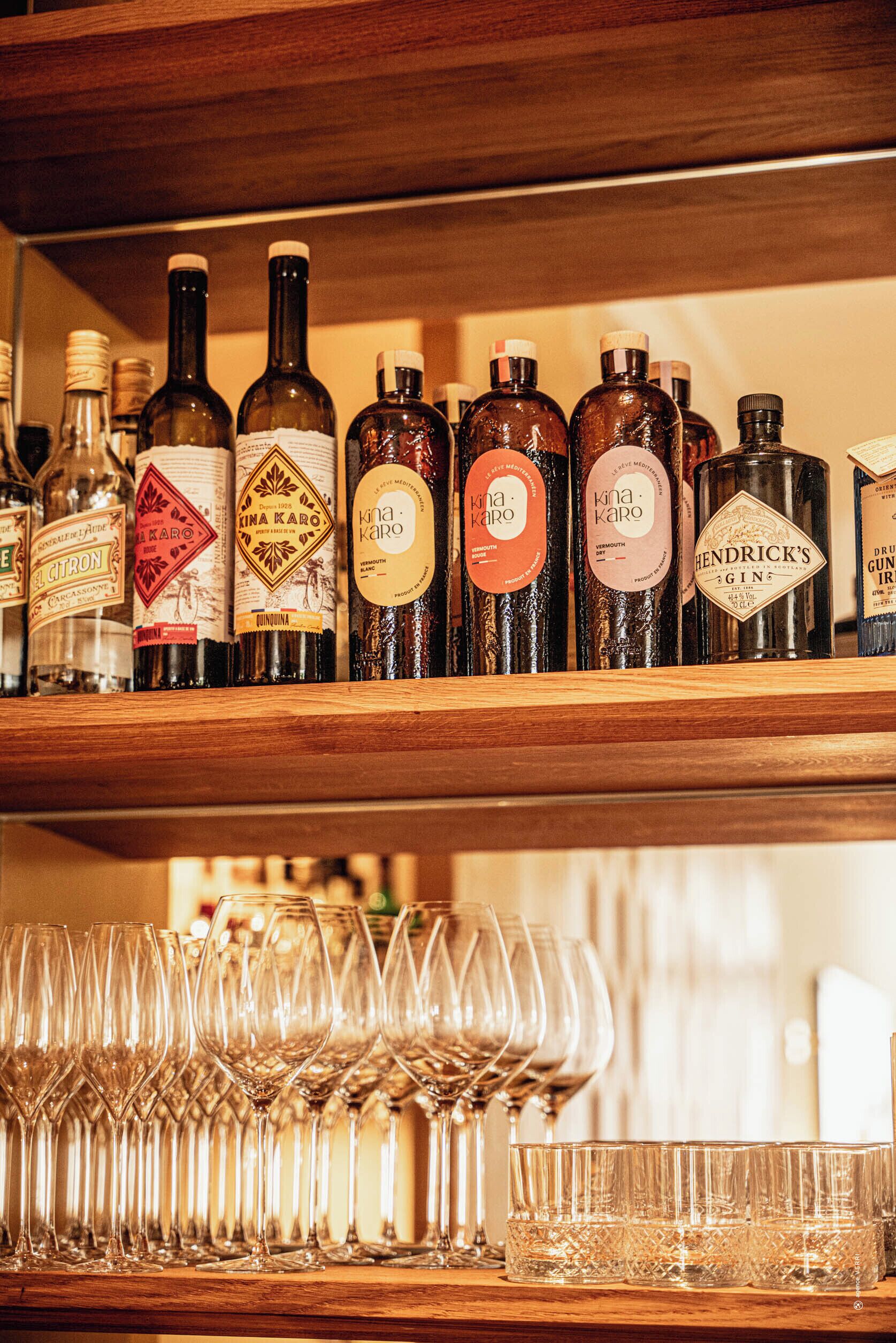 A shelf with various bottles of alcohol and a row of empty wine glasses below.