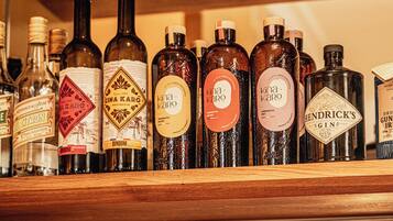 A shelf with various bottles of alcohol and a row of empty wine glasses below.