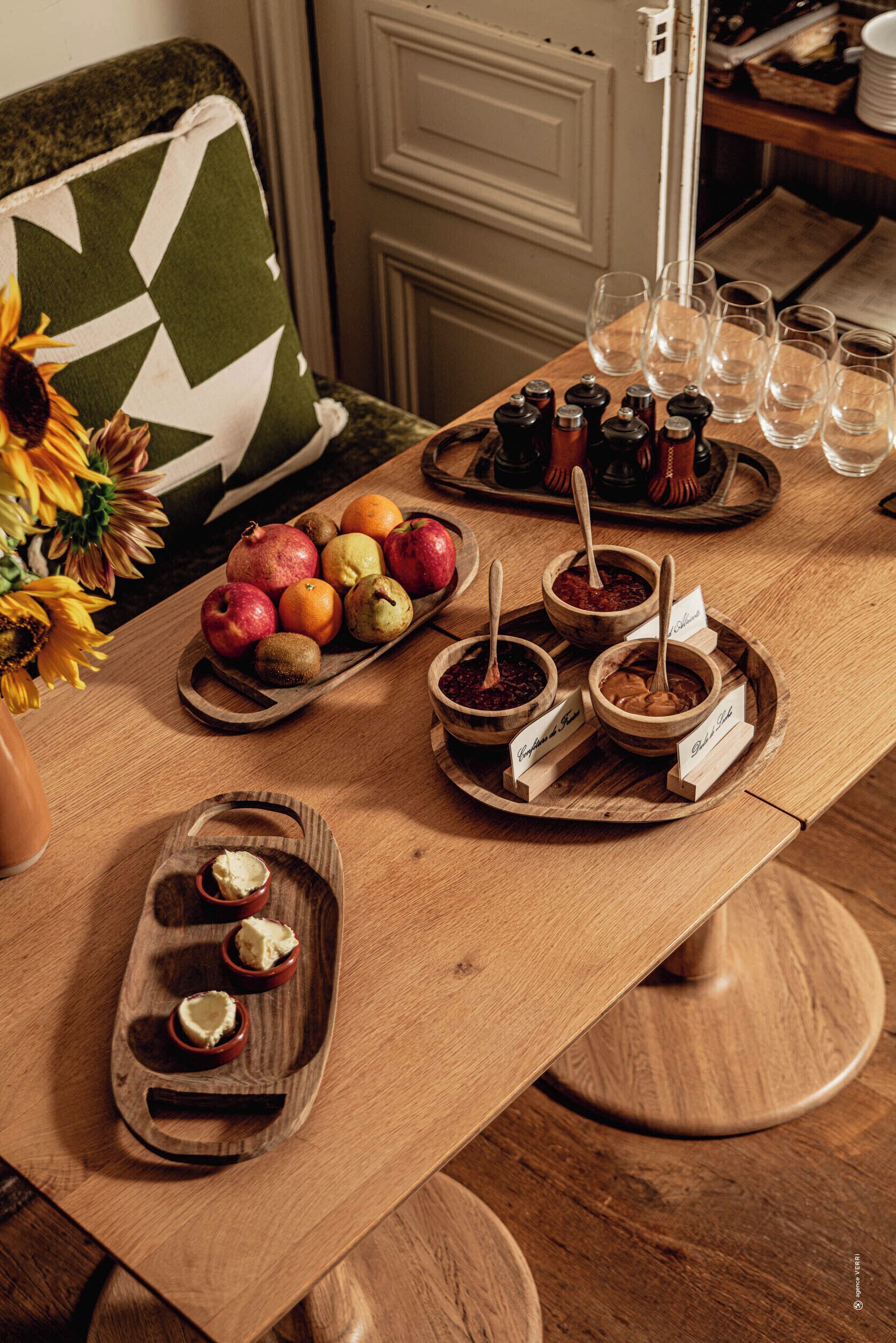 A wooden table with various food items and condiments, a vase with sunflowers, and a green and white patterned pillow on a couch.