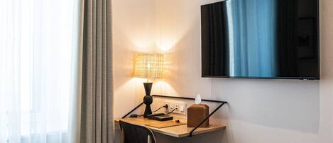 A hotel room with a bed, a desk with a lamp, a television, and a trash bin.