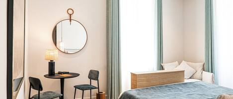 Una habitación de hotel con una cama, un escritorio con dos sillas, un espejo redondo y una lámpara.