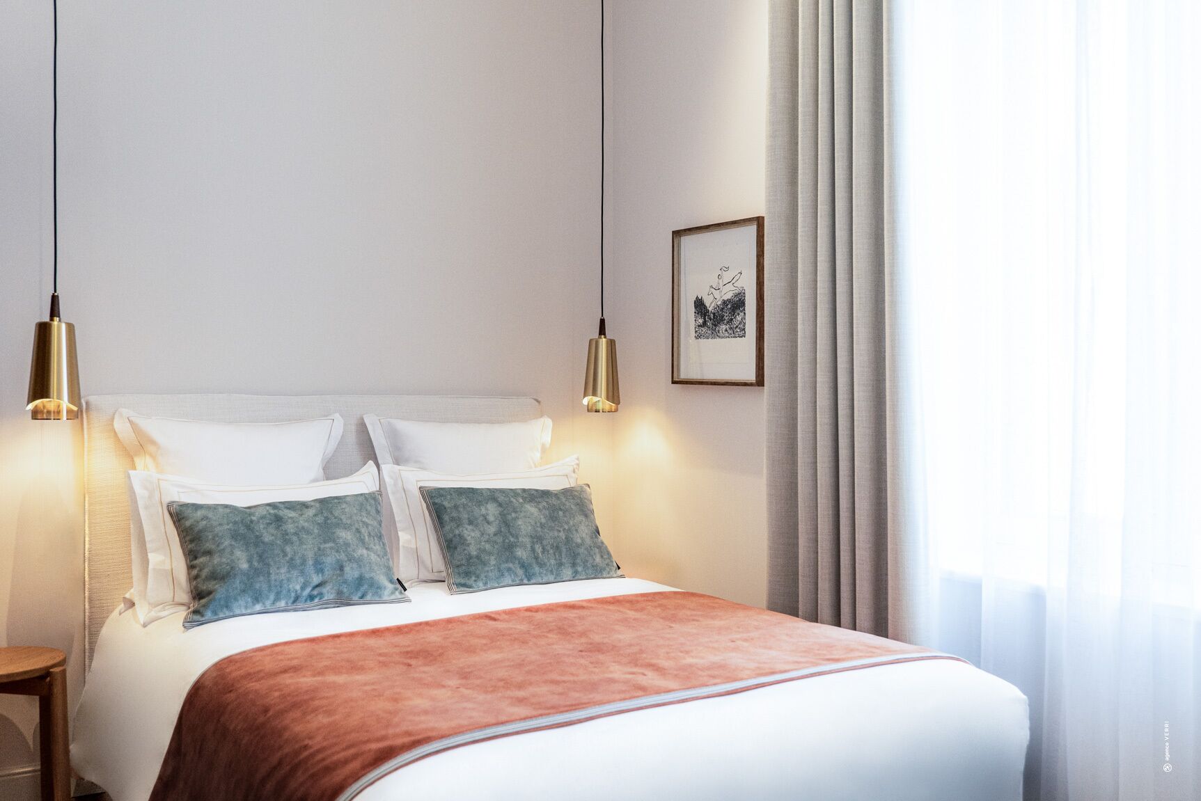 Una cama bien tendida con una manta blanca y marrón, dos almohadas y dos lámparas de noche.