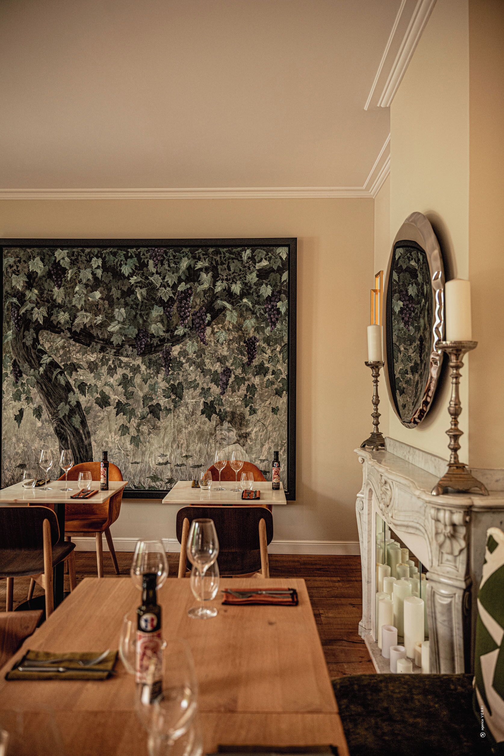 Un espace repas agrémenté d’une grande fresque murale, d’une cheminée avec des bougies et d’un miroir placé au-dessus.