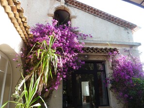 A building with a tiled roof, a doorway, and purple flowering plants.