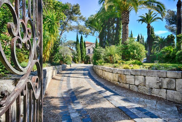A paved pathway leading to a building, surrounded by stone walls and lush greenery.