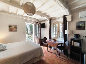 A bedroom with a bed, a wooden table, chairs, a desk with a lamp, and a TV.