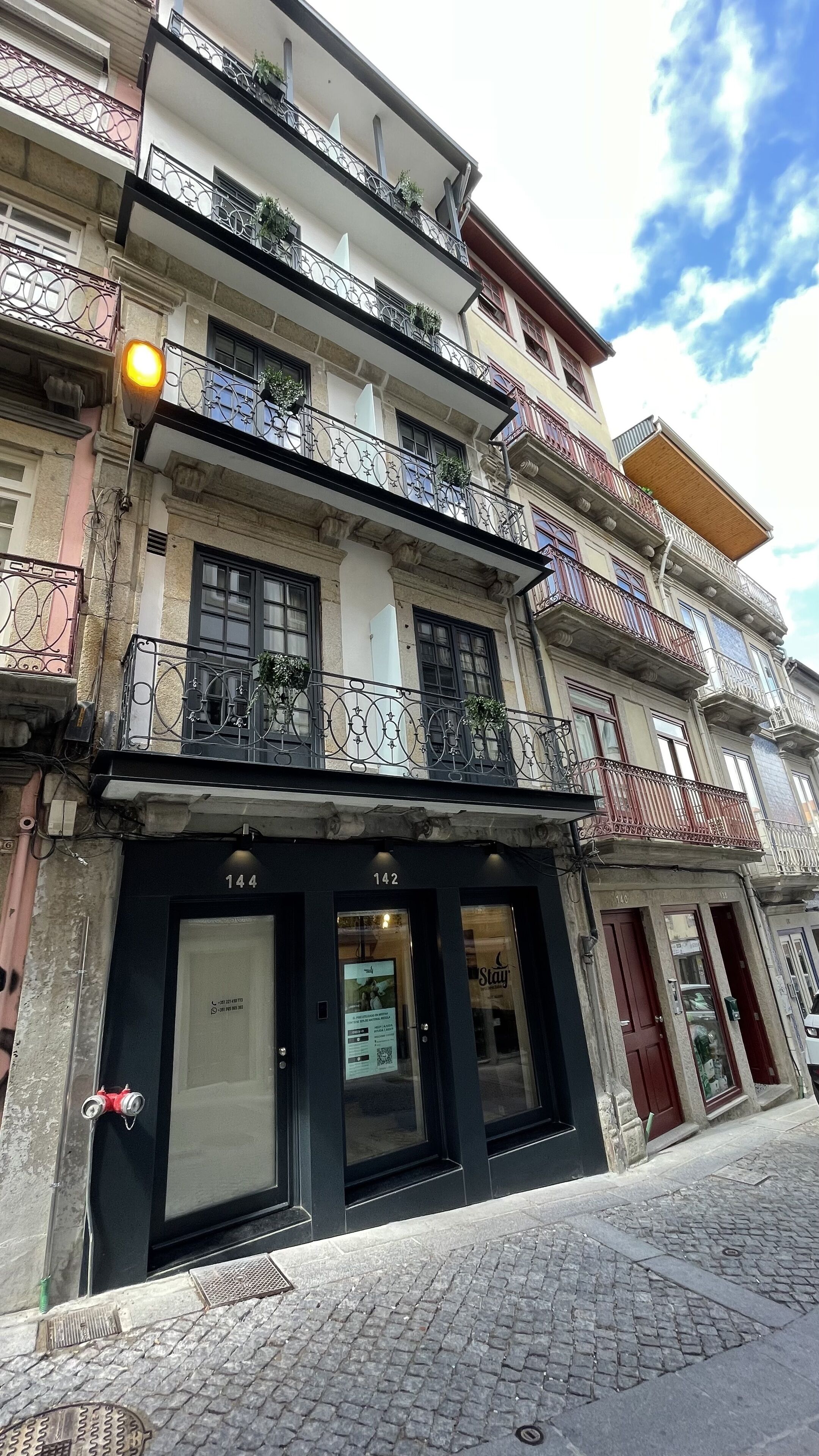 Um edifício de vários andares com varandas, uma loja com uma placa e uma rua de paralelepípedos.