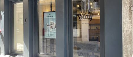 A hotel entrance with a glass door, a sign for 'myStay' with a check-in instruction, and a visible address '144'.