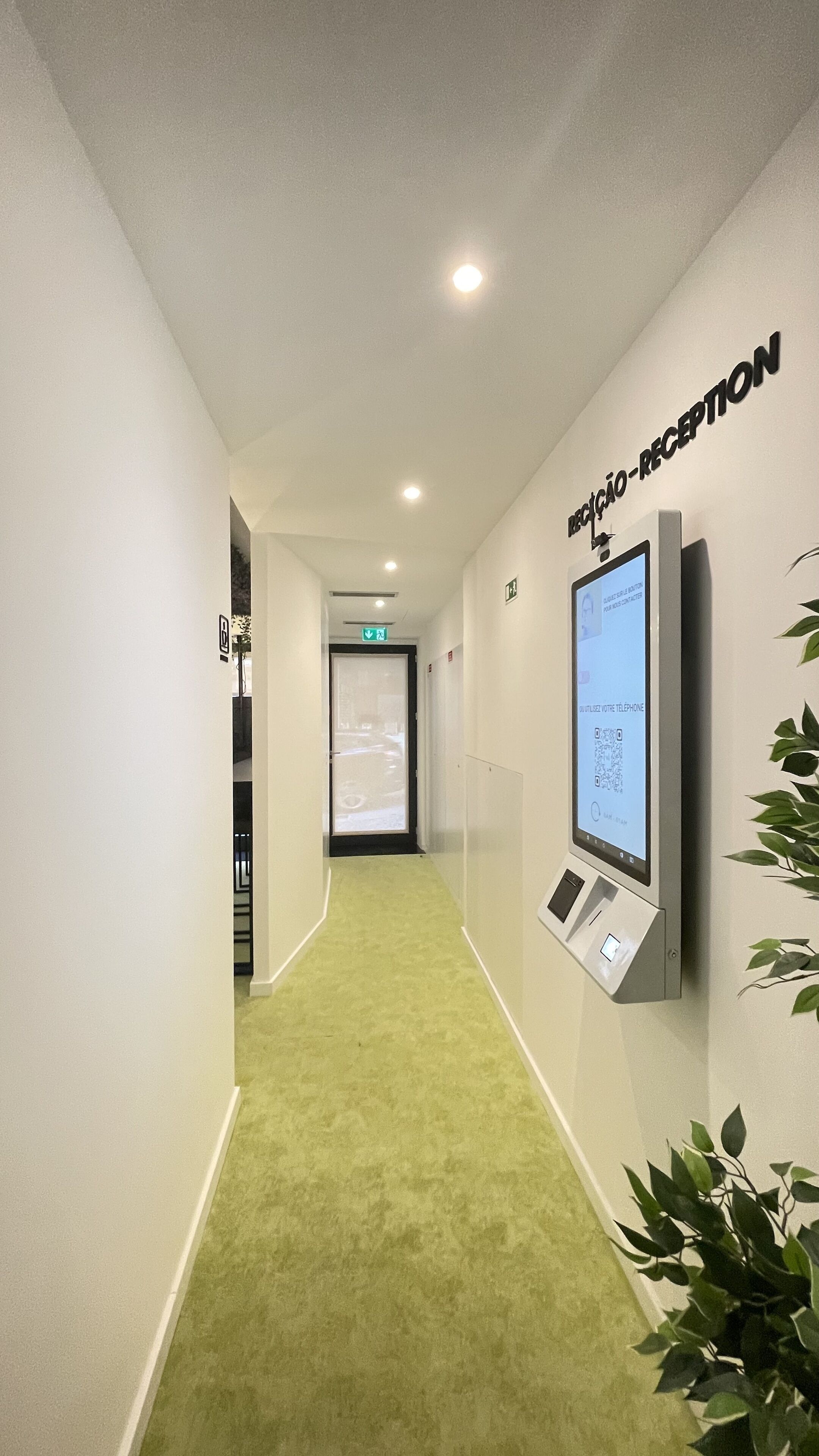 A reception area with a green carpet, a digital screen displaying a map, and a QR code.