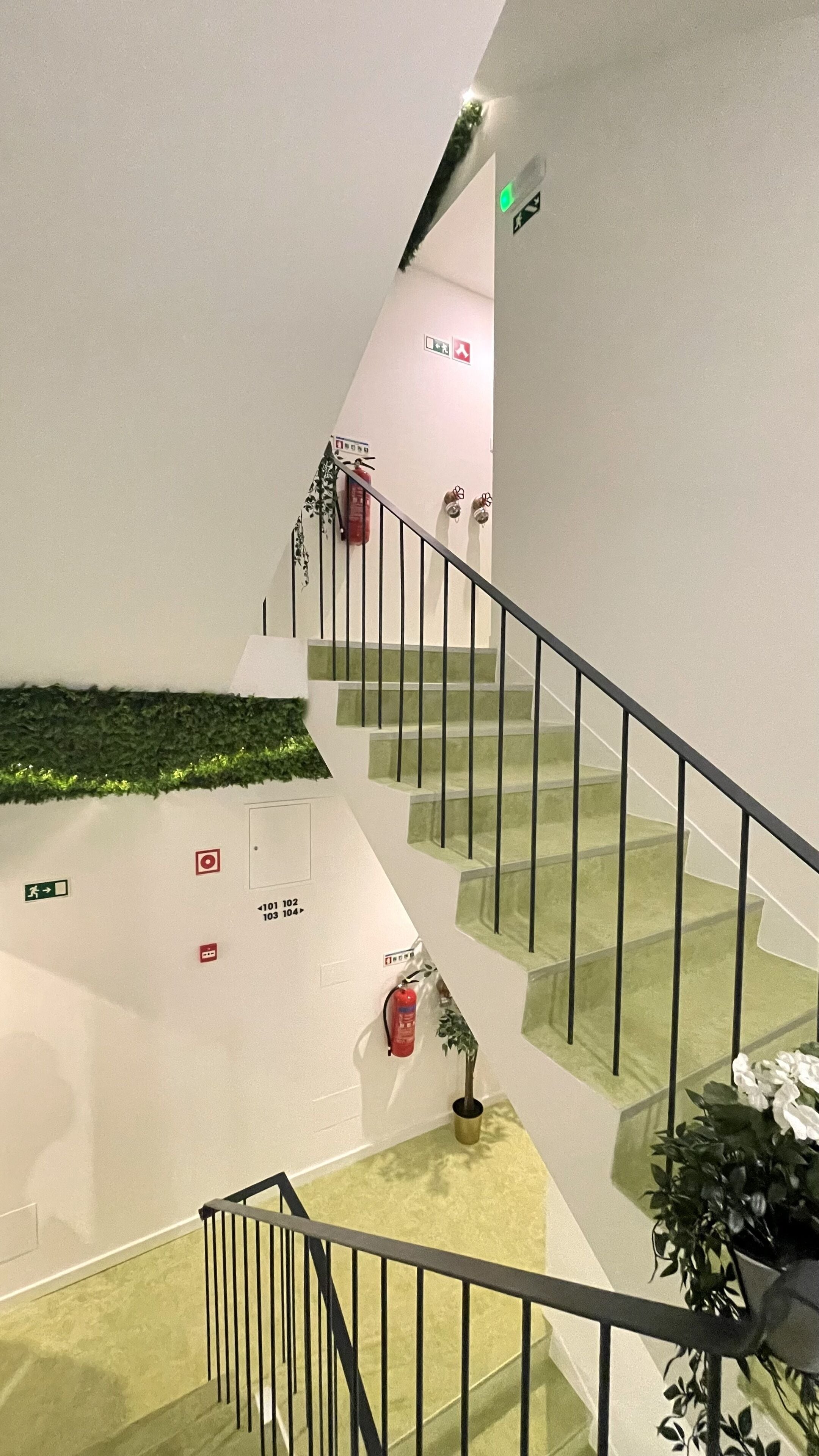 Una escalera con peldaños verdes, barandillas negras y un extintor montado en la pared.