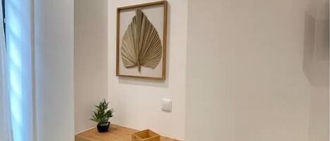 Um quarto compacto com uma escrivaninha de madeira, um banquinho pequeno, uma obra de arte emoldurada e um vaso com planta.