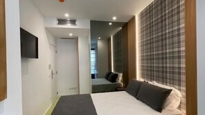 A modern hotel room with a large bed, a bedside table, a flat-screen TV mounted on the wall, and a green carpet. - MyStay Porto São Bento (Porto)
