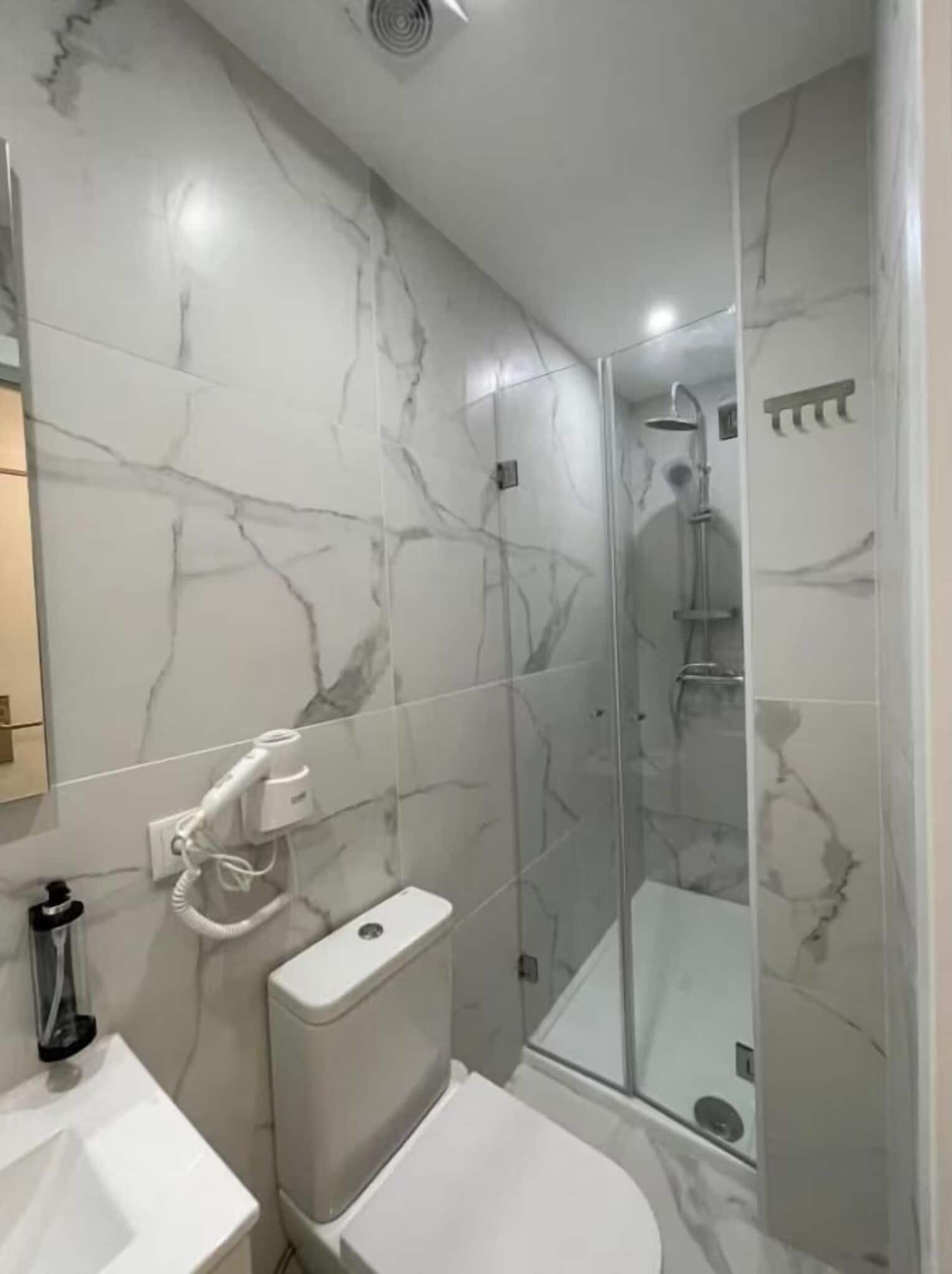 A bathroom with marble tiles, a toilet, a sink, and a glass-enclosed shower area.