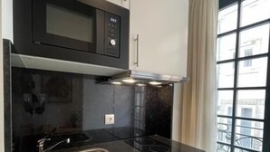 A compact kitchen with a black microwave, stainless steel sink, and white cabinets. - MyStay Porto São Bento (Porto)