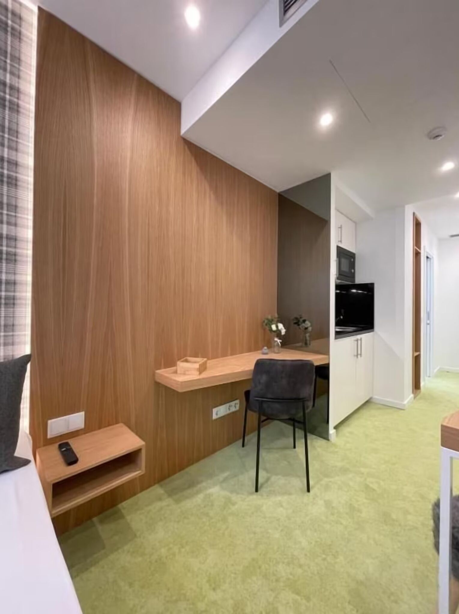 Une pièce compacte avec un mur d’accent en bois, une petite kitchenette, un bureau avec une chaise et un lit.