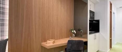 Une pièce compacte avec un mur d’accent en bois, une petite kitchenette, un bureau avec une chaise et un lit.