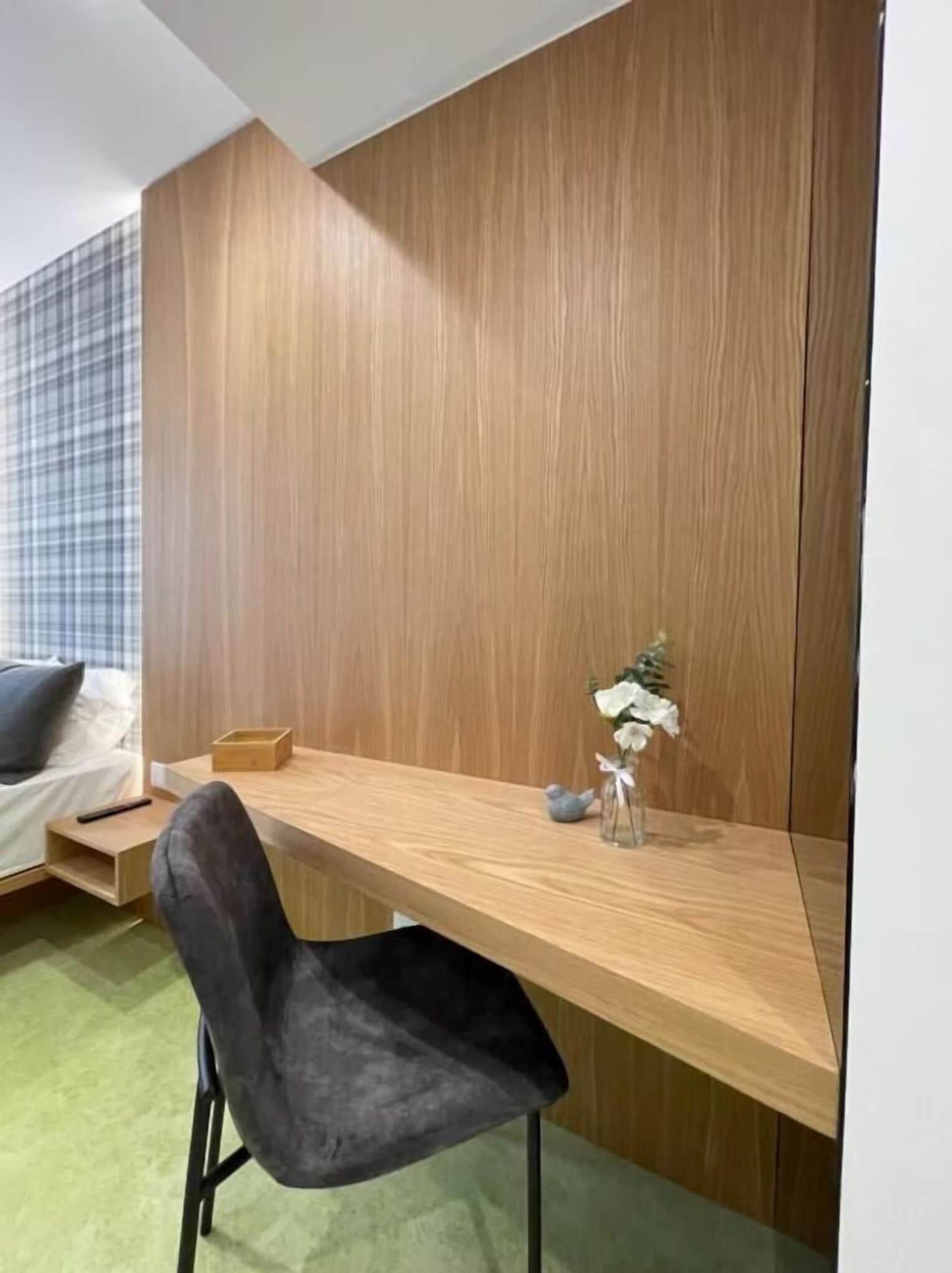 A compact room with a wooden desk, a black chair, a small table, and a vase with flowers.