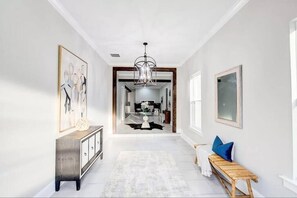 Un couloir avec un banc en bois, un tapis blanc et un lustre.