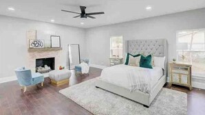 A bedroom with a large bed, a ceiling fan, a fireplace, and a nightstand. - Entire Home- Immaculate 5 bedrooms Sleeps 13 (Memphis)