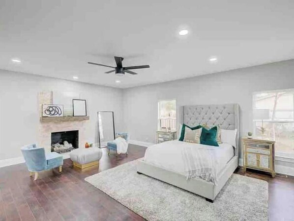 Une chambre avec un grand lit, un ventilateur de plafond, une cheminée et une table de chevet.