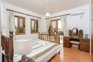 Ein Schlafzimmer mit Bett, Schreibtisch, Stuhl, Kommode und Balkonblick.