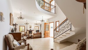 Amplia sala de estar con techo alto, una escalera con barandillas de metal ornamentadas y una chimenea.