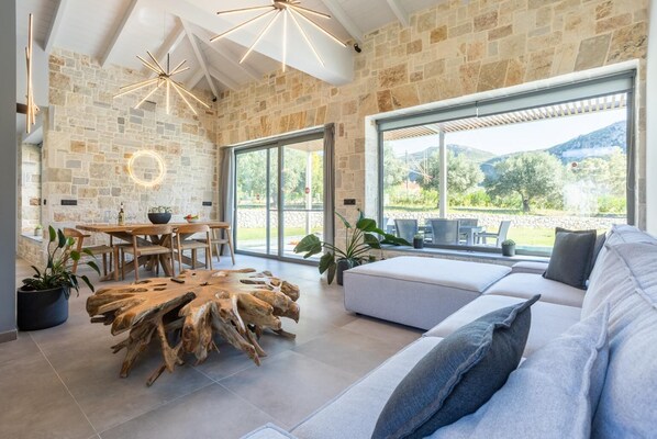 Amplia sala de estar con pared de piedra, una mesa de centro de madera, un sofá con cojines y un gran ventanal con vistas al exterior.