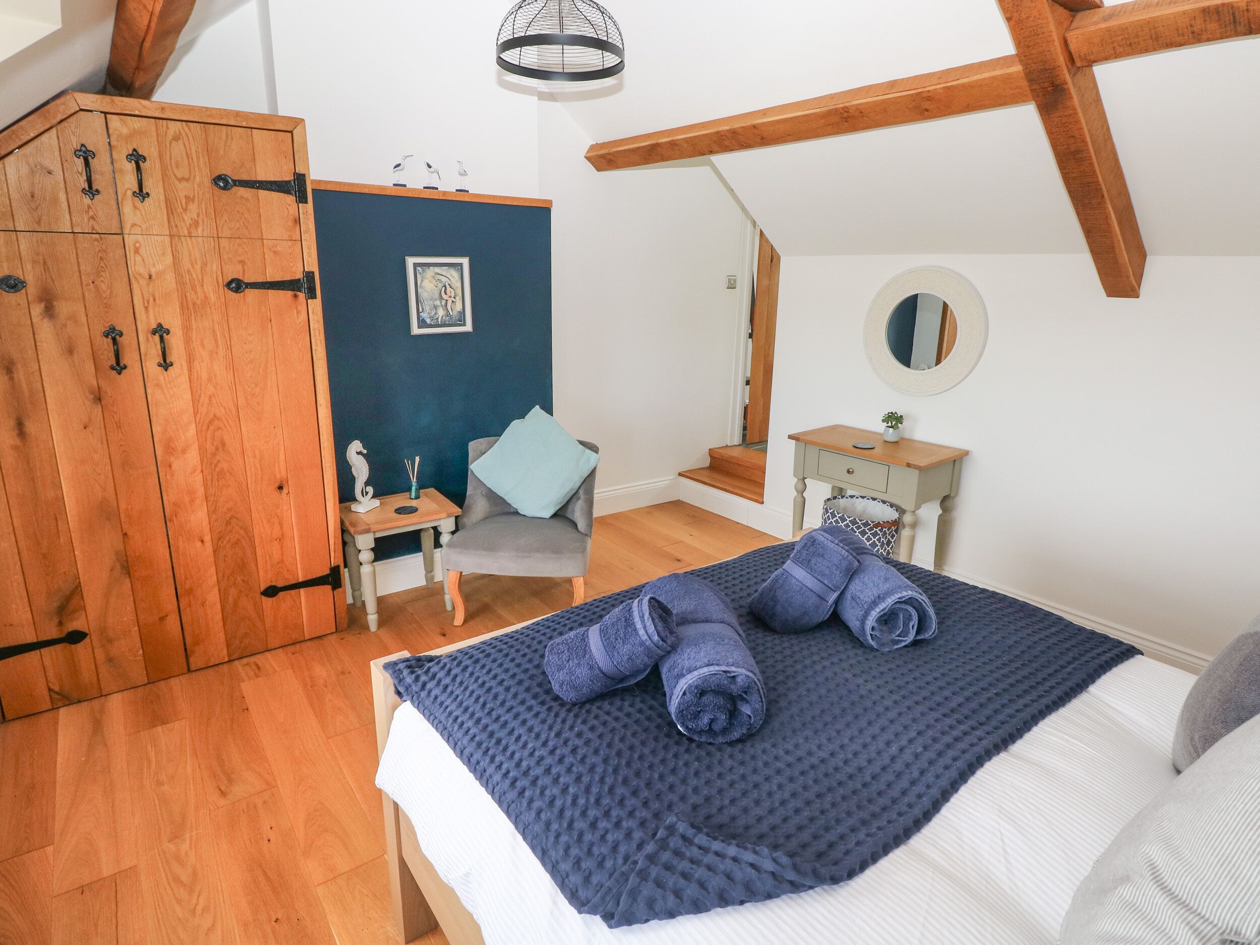 Een slaapkamer met een bed, een houten garderobe, een stoel, een klein tafeltje en een spiegel.