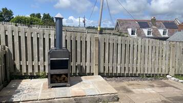 A stone patio with a wood-burning stove, a wooden fence, and houses in the background.