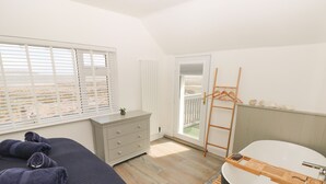 Une chambre à coucher comprenant un lit, une commode, une fenêtre avec des stores, une salle de bain avec une baignoire et une échelle en bois.