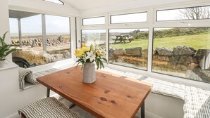 Une pièce moderne avec une table et un banc en bois, de grandes fenêtres offrant une vue sur la plage et les rochers.