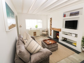 Ein modernes Wohnzimmer mit Sofa, Hocker, Kamin, Fernseher und einem Fenster mit Blick.