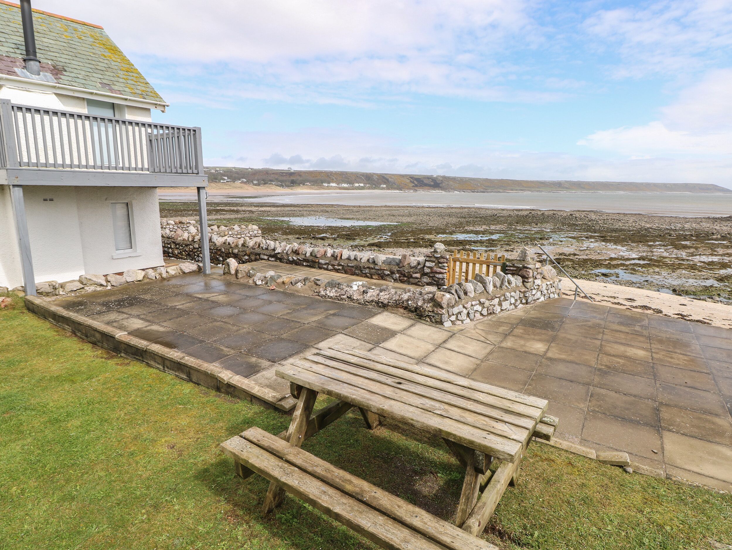 Une terrasse avec un banc en bois, un mur de pierre et une vue sur la mer.