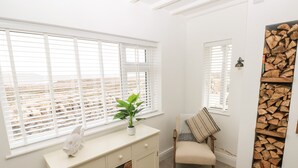 Une pièce avec une armoire blanche, une plante en pot, une chaise recouverte d’une couverture et une étagère murale où sont exposées des bûches de bois.