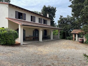 Une maison à deux étages dotée d’un patio couvert, d’une allée en gravier et d’un petit jardin.