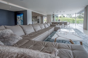 Uma sala moderna com um amplo sofá modular bege, uma mesa de centro de vidro e um espaço de jantar com mesa e cadeiras.
