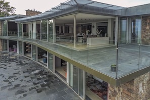 Uma casa moderna com varanda de vidro, fachada de pedra e área externa coberta com assentos.