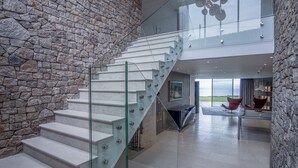 A modern staircase with glass railings, a stone wall, and a view of the outdoors. - Bryn House - 5 Bed Home - Penmaen (Swansea)