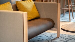 Een moderne bank met een bruine leren zitgedeelte en twee mosterdgele kussens, geplaatst in een eigentijdse kamer met houten meubels en een kamerbreed tapijt.