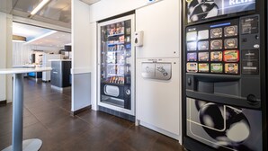 A modern hotel lobby with a self-service beverage machine and a refrigerated display case. - B&B HOTEL Calais Terminal Cité de l'Europe 2 étoiles (Coquelles)