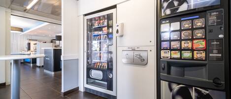 A modern hotel lobby with a self-service beverage machine and a refrigerated display case.